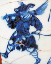 An image of a piece of ceramic art depicting a dark-furred, pig-headed monk wearing a robe and carrying a rake.